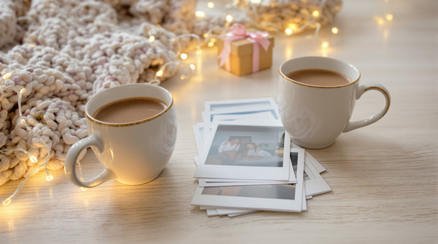 Deux tasses de chocolat chaud côte à côte, des photos souvenirs et un cadeau emballé sur une table de Noël